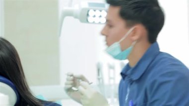 Genç başarılı dişçi portresi. Diş hekimi aracını seçer ve diş sandalyede oturan diş hastanın muayene başlar