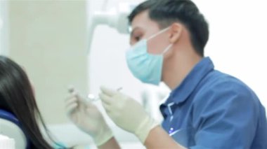 Genç başarılı dişçi portresi. Doktor maskesi aracını seçer ve diş hastaya incelenmesi başlar, sonra özel bir lamba yanar ve muayene devam ediyor