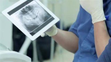 Bir resepsiyonda diş hekimi. Dişçi dişlerini ona tablet röntgende gösterir. Close-Up diş tablette bir x-ışını fotoğrafı.