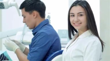 Kız-Yardımcısı dişçi portresi. Şef dişçiyle oturan kız. Kız-Yardımcısı gülümseyen ve başparmak üzerinde arka plan diş hekimi