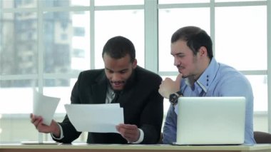 İş sözleşmeleri. İki başarılı iş adamı resmi bir iş ofisinde dizüstü bilgisayarda çalışırken iş adamı elinde belgeleri tutuyor..