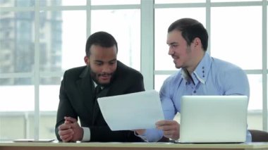 İş akışı. İki başarılı iş adamı resmi bir iş ofisinde dizüstü bilgisayarda çalışırken iş adamı elinde belgeleri tutuyor..