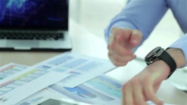 İş adamının saatini yakından takip ederken, iki başarılı işadamı resmi giyim ve dizüstü bilgisayarda iş yerinde her birine karşı masada otururken.