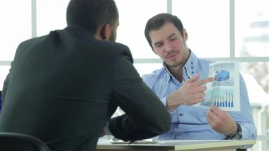 İş raporlama. İki emin işadamı pazarlığı oturan ofiste masa ve mali rapor göz önünde bulundurun. İş adamları formal giyim giyinmiş