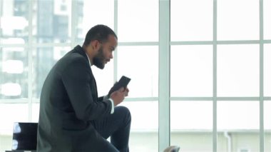 Gelen aramaları kontrol. Bir cep telefonu elinde tutarak ofis masasında oturan kendine güvenen iş adamı. Formal giyim giyinmiş işadamı
