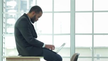 Afrika işadamı masa başında oturan dizüstü bilgisayarda çalışır. Kendine güvenen işadamı dizüstü elinde tutarak ofis masasında oturuyor. Formal giyim giyinmiş işadamı