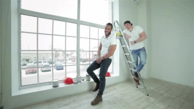 Güzel iş. İki genç inşaatçılar boya merdivenle ayakta el başparmak gösterilen kutular