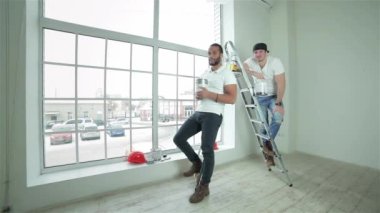 Taşıma ve onarır dairede. İki genç inşaatçılar boya merdivenle ayakta el başparmak gösterilen kutular