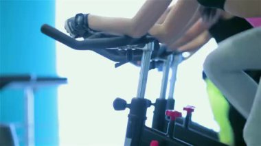 Grup fitness egzersiz bisiklet sürme. Sporcu kız spor sabit bir bisiklet üzerinde pedal. Yakın çekim görünümü simülatörleri