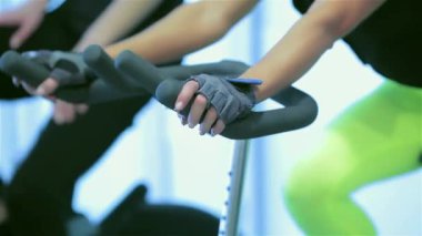 Grup fitness egzersiz bisiklet sürme. Sporcu kız spor sabit bir bisiklet üzerinde pedal. Yakın çekim görünümü simülatörleri