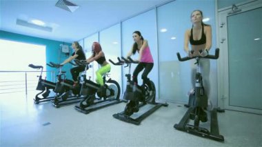 Spor salonunda grup egzersizleri. Pedal arkadaşlar spor ve spor salonunda bir sabit bisiklet önünde görünüyor. Sporcular spor kıyafetler giymiş.