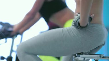 Spor salonunda fitness dersleri. Atletik kız üzerinde simülatörü kadar onun dört kız sporcular spor sabit bir bisiklet üzerinde pedal pedal. Spor karın metrelik yakın çekim