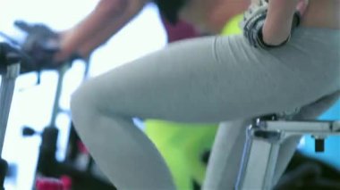 Spor salonunda fitness dersleri. Atletik kız üzerinde simülatörü kadar onun dört kız sporcular spor sabit bir bisiklet üzerinde pedal pedal. Spor karın metrelik yakın çekim