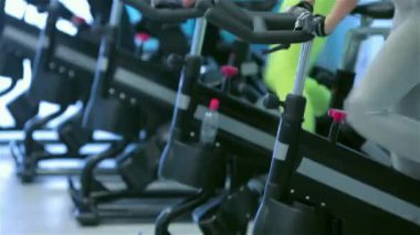 Spor olarak çalışma. Pedal arkadaşlar spor ve onların arkadaşları sporcular Bisiklet arka planda bisikletine iken spor salonunda bir sabit bisiklet önünde görünüyor