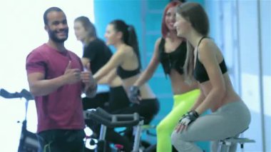Sağlıklı spor. Arkadaşları salonunda sporcuların ve spor onların arkadaşları dahil ederken bir başparmak gösterilmesini ve sabit bir bisiklet üzerinde pedal fotoğraf makinesi içine bakmak