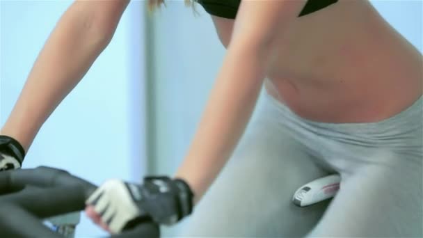 ジムでのフィットネス クラス ジムでエアロバイクのペダル ガールフレンド選手までシミュレータでペダリング運動女の子 スポーツおなかのクローズ アップ — ストック動画
