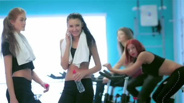 健康的なスポーツです 少女選手がスポーツに関与し 静止した自転車のペダルの友達ながら呼び出しを受信します — ストック動画