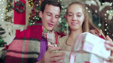 Noel mobilyalı bir odada hediyeler tutan kazak ve eşarp giymiş sevgi dolu bir çift. Aşık adam genç çift ve evde kazak ve eşarp giyen güzel kız.