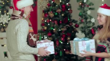 Noel mobilyalı bir odada hediyeler tutan kazak ve eşarp giymiş sevgi dolu bir çift. Aşık adam genç çift ve evde kazak ve eşarp giyen güzel kız.