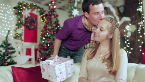 愛するカップルは クリスマスの家具付きの部屋で贈り物を保持するセーターとスカーフを着て 愛の男と自宅でセーターとスカーフを着てかわいい女の子の若いカップル — ストック動画