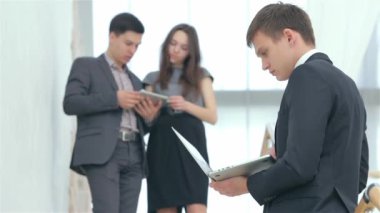 Ön planda, defteri olan genç bir adam. Arka planda genç bir çift işadamları