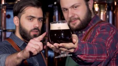 Canlı bir bira fabrikası ortamında, iki yetenekli bira üreticisi canlı bir tartışmaya giriştiler, bir bardak zengin, koyu bira sergilediler. Odaklanmış ifadeleri ve parıldayan camları sanatın sanatını ön plana çıkarıyor.