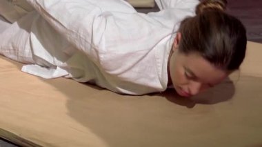 Saf mutluluğa kapılmış dingin genç bir kadın, geleneksel Tayland masajından zevk alıyor. Yetenekli bir masör nazikçe sırtını geriyor. Yumuşak ışıklandırma ve sakinleştirici ile süslenmiş sakin bir spa ortamı.