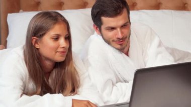 Keyifli bir çift, rahat bornozlara sarılmış, kameraya ışıl ışıl gülümsüyor lüks balayı süitlerinde. Yatakta rahat bir şekilde uzanıyorlar, dizüstü bilgisayarlarında film izlerken gülüyorlar.