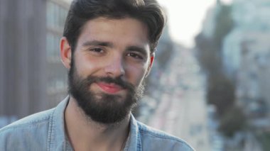 Kamerada bakımlı sakalları olan çekici bir genç adam şehrin hareketli bir arka planına karşı koyuyor. Rahatlamış tavrı ve kendinden emin gülüşü olumlu bir hava yayıyor ve izleyicileri kendisine davet ediyor.