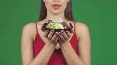 Çekici, çekici dudakları olan genç bir kadının büyüleyici yakın çekimi elinde taze salatayla neşeyle onları yalıyor. Bu cezbedici görüntü sağlık ve şehvetin bir karışımını yayıyor.