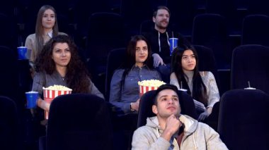 Aralarında iki erkek ve dört kızın da bulunduğu canlı bir grup genç arkadaş tiyatroda sinematik bir deneyime daldı. Ellerinde patlamış mısır ve yanlarında içkilerle, ifadeleri neşe saçıyor.