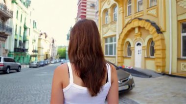 Uzun kahverengi saçlı, genç ve çekici bir kadın neşe ve macera saçan canlı, tarihi bir kasabada rahatça yürüyor. Yazlık kıyafetleri ve tasasız tavırları mükemmel bir şekilde yansıtıyor.