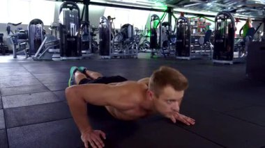 Odaklanmış genç beyaz bir atlet, kaslı vücudunu sergileyerek şık bir spor salonunda şınav çekiyor. Yüzüne kazınmış kararlılıkla, gücünü ve disiplini somutlaştırıyor, sınırlarını zorluyor.