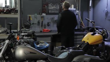 Şık sakallı, genç bir beyaz adam motorsikletinin üzerine eğilmiş, iyi donanımlı bir atölyede ingiliz anahtarıyla vidaları söküyor. Sahne tutkunun özünü yakalar.