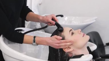 Şık bir kuaförde, yetenekli bir güzellik uzmanı dingin genç bir kadının saçını nazikçe yıkıyor ve keyifli bir atmosfer yaratıyor. Yatıştırıcı su, uzun ve güzel kilitlerinin üzerinde çağlarken...