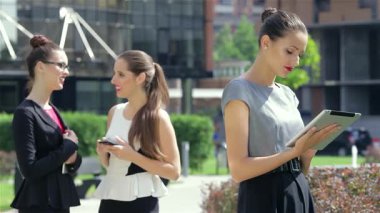 Canlı bir şehir ortamında, dengeli genç bir iş kadını tabletinde haberleri okuyarak profesyonelliğini yayıyor. Bu arada, şık meslektaşları da dinamik bir atmosfer sergileyerek bir ışık anı paylaşıyorlar.