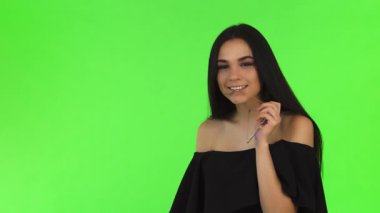 Cazip, siyah elbiseli genç bir kadın, gözlükleriyle neşeli bir şekilde poz veriyor, parlak yeşil renkli arka planına karşı kendine güvenini yayıyor. Bu büyüleyici sahne,