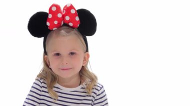 Beyaz tenli, dalgalı sarı saçlı çekici bir kız işaret parmağını dudaklarına getirip sessizlik işareti veriyor. Şirin çizgili bir tişört ve enfes bir Minnie Mouse saç bandı giymişti.