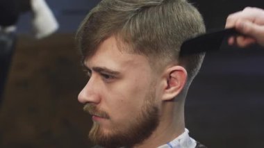Bu yakın plan, yetenekli bir berberin elektrikli makasla saçını ustalıkla keserken kendine güvenen genç bir adamı yakalıyor. Atmosfer canlı ve modern, sanatsal özelliklerini sergiliyor.