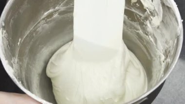 Büyüleyici bir yakın plan, profesyonel bir şefin parlak bir metal kasede lezzetli vanilya kremini ustaca çırptığını, yemek sanatını somutlaştırdığını gösteriyor. Kremanın yumuşak, kadife gibi dokusu vaad ediyor.