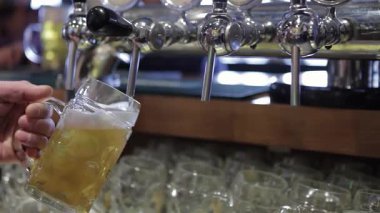 Yetenekli bir barmen, buzlu bardağı altın birayla doldurur ve kenardan dökülen köpüğü gösterir. Bu canlı sahne gece hayatının özünü yakalar, her döküm neşe getirir ve