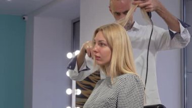 Neşeli genç bir kadın saçını modern bir kuaförde şekillendirirken mutluluk saçıyor, profesyonel kuaförünün sanatını sergiliyor. Canlı atmosfer ve parlak ışık güçlendiriyor.