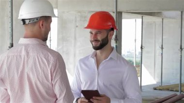 Gıcır gıcır beyaz bir gömlek ve turuncu bir şapka giyen sakallı bir inşaat mühendisi, hareketli bir inşaat sahasında takım çalışması yapan bir meslektaşıyla canlı bir tartışmaya girişiyor. Şey...