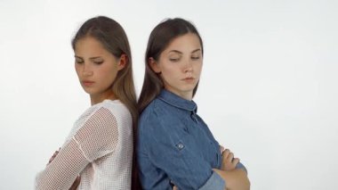 İki genç kadın sırt sırta vermiş, kollarını kavuşturmuş, hayal kırıklığıyla dolu ifadeler, bir kavga sonrası gerginlik sergiliyorlar. Çelişkili duyguları arkadaşlığın karmaşıklığını vurgular.