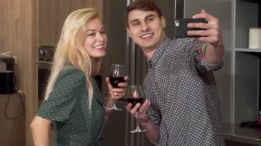 Neşeli bir çift, ellerinde kırmızı şarap kadehleriyle şık yeni dairelerinde sevgililer gününde aşklarını kutlarken selfie çekiyorlar. Sıcak ortam ve modern dekor için mükemmel bir zemin oluşturur.