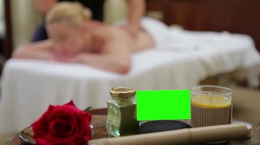 Huzurlu bir sahne, yetenekli bir terapistin sırtında çalışması gibi, rahat bir şekilde masaj masasında uzanan güzel bir genç kadını yakalar. Etrafı aromatik mumlar gibi sakinleştirici elementlerle çevrili.