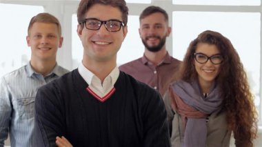 Üç genç erkek ve bir kadından oluşan canlı bir grup modern bir ofiste gururla duruyor, güven ve takım çalışması yayıyorlar. Gözlüklü esmer adam, kollarını kavuşturdu, yolu açtı, neşeli adam