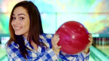 Çekici esmer bir kız neşeli bir şekilde yüzüne canlı bir bowling topu tutuyor, neşe ve heyecan saçıyor. Bu yakın plan, şık bir kareli gömlekle neşeli bir beyaz kadın yakalıyor.