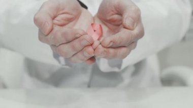İlgili bir doktor ellerinde meme kanseri farkındalığını sembolize eden, umut ve destek saçan pembe bir kurdeleyi nazikçe beşikte tutuyor. Bu dokunaklı görüntü, erken teşhis ve benliğin önemini vurgular.