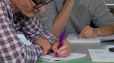 Kendini işine adamış, şık gözlükler takan genç bir adam, rahat bir kütüphane atmosferiyle çevrili ders kitabında derinden notlar yazmakla meşgul. Neşeli gülüşü öğrenmenin verdiği hazzı yansıtıyor.